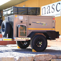 Two compactly folded down tent-trailers in front of a building with a sign saying nasc North American Safari Company