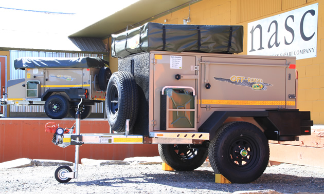 Two compactly folded down tent-trailers in front of a building with a sign saying nasc North American Safari Company