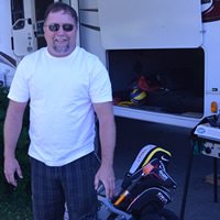 Smiling man in sunglasses, with golf clubs at hand and an RV in the background