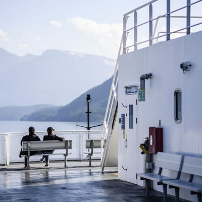 Two people sitting on bench on deck of ferry. 