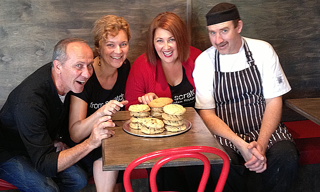 Two smiling couples appear ready to pounce on assorted goodies on the table in front of them