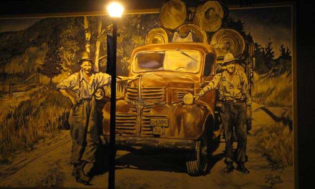 a painted mural on the side of a building at night lit by a vintage streetlight; mural is of two men standing beside an old truck