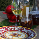 Attractive red and yellow designs on china is set out in front of ice tea, an apple, and glasses of wine to create an appealing camp setting.