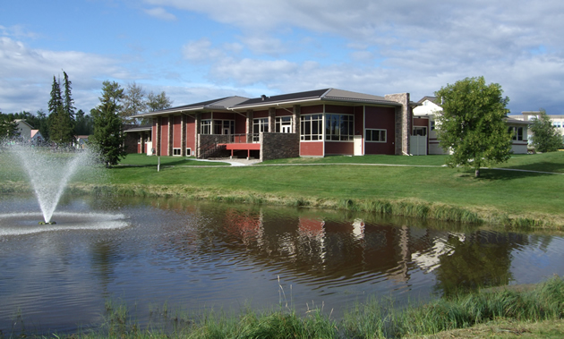 An attractive dark red building stands beneath a blue sky, on green grass and above a pond and fountain.