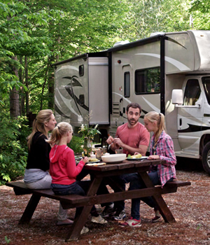 Family of four at a campsite picnic table with a motorhome in the background