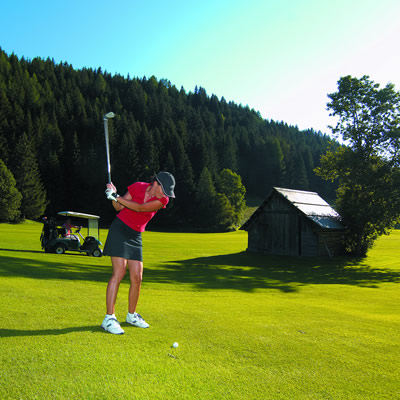 A woman golfing with treed hillside in background.  