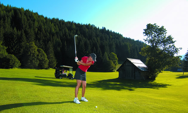 A woman golfing with treed hillside in background.