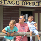 A man with two children stand outside a building bearing the sign 