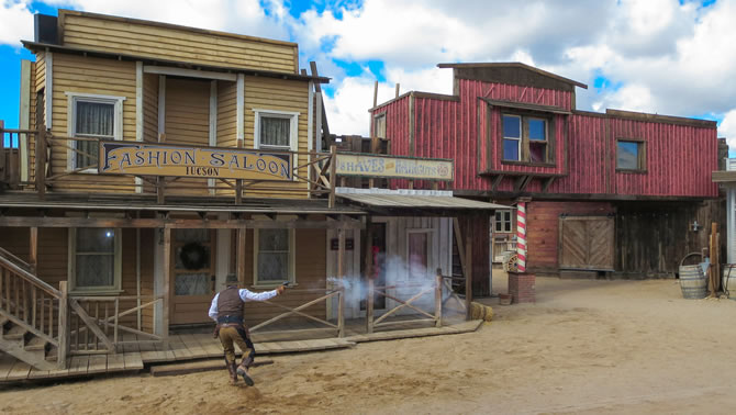 A man is running while shooting a gun in a simulated gunfight in an Old Western town.