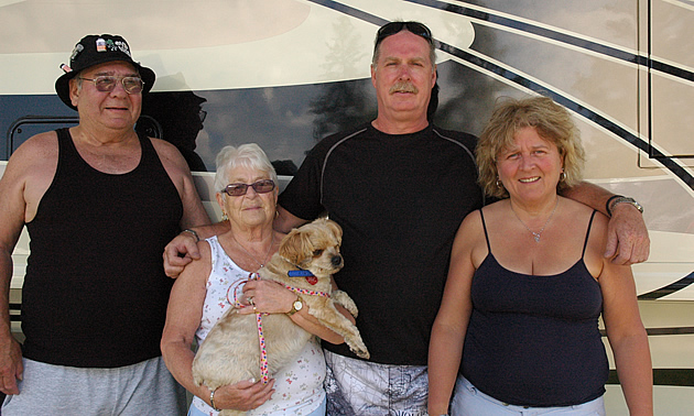 Two couples and one small dog stand beside their motorhome