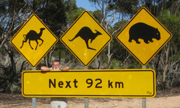 Man poses next to a road sign of a camel, a kangaroo and a wombat in Australia