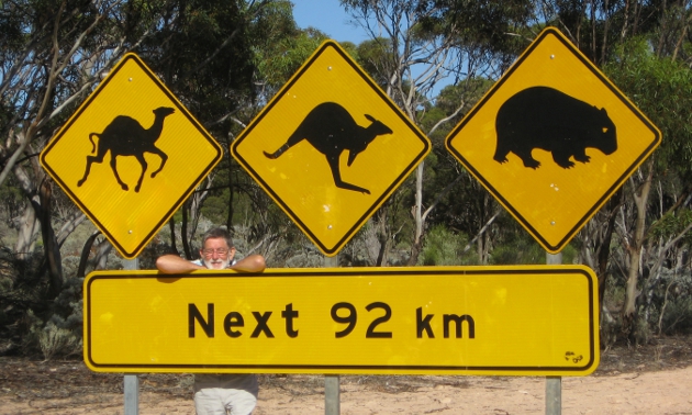Man poses next to a road sign of a camel, a kangaroo and a wombat in Australia
