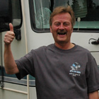 Smiling man does a thumbs-up, standing in front of his motorhome.