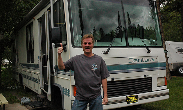 Smiling man does a thumbs-up, standing in front of his motorhome.
