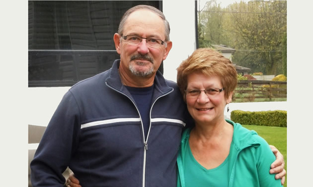 A couple stand, arms around each other, smiling for the camera in front of their RV.