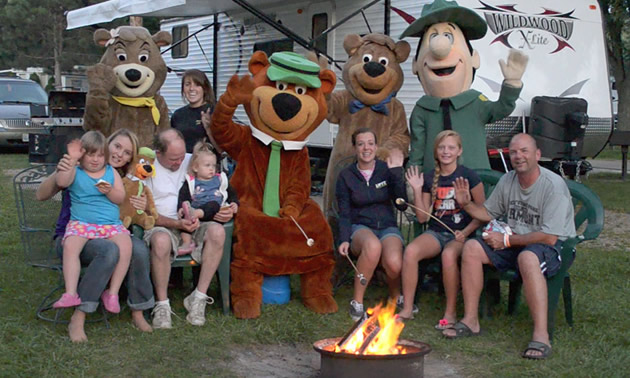 Jellystone guests and costumed characters around a campfire.
