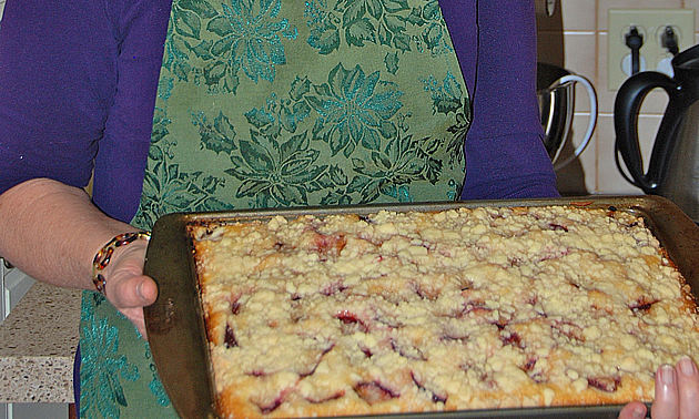 Hands hold a baking sheet containing a fruit crumble.