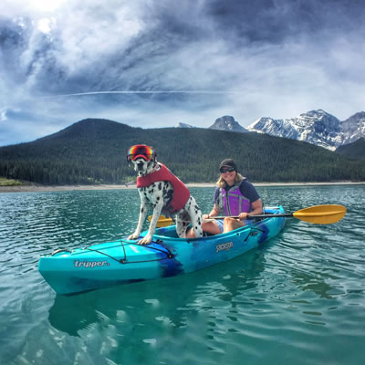 Traveler the Dalmatian is standing at the front of a kayak with Rashelle Elburg holding a paddle.