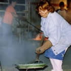 a woman using a large pitchfork to put a piece of raku pottery into a bed of straw to cool after being fired