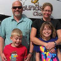 Couple with two young children and a large RV behind them