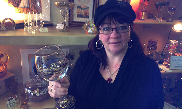 Woman in a shop holding a handpainted glass. 