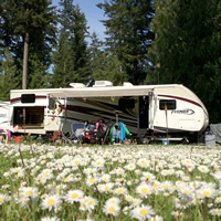 Two girls run around in the front of a set up RV.