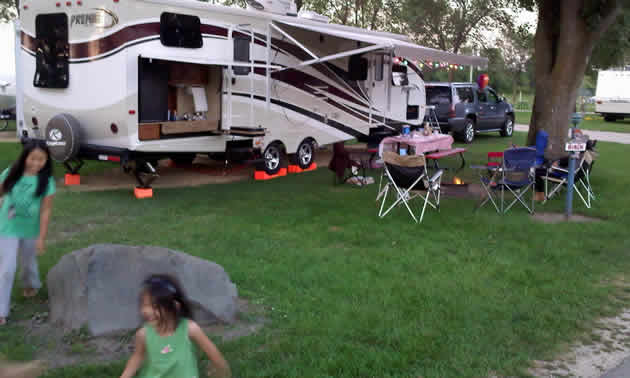 Two girls run around in the front of a set up RV.