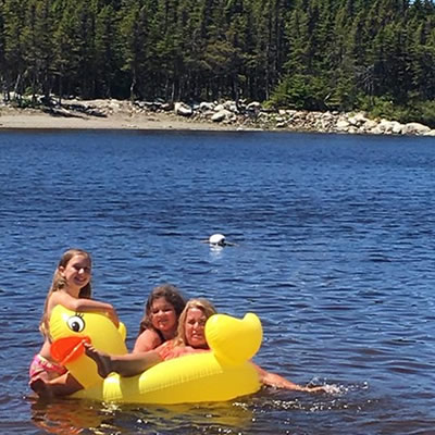 Woman and two kids floating on inflatable duck in water. 