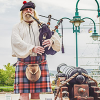 A bagpipe player in traditional dress stands between two cannons.