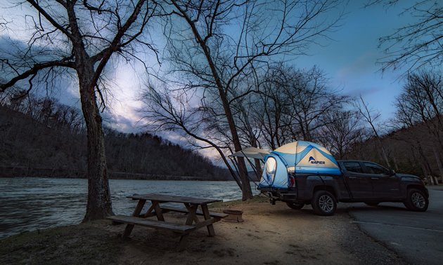 A lantern lit Truck Tent by a river at night.