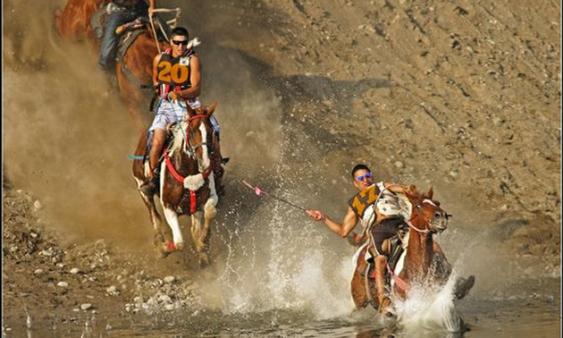 Picture of horses and riders coming down a steep bank beside a river. 