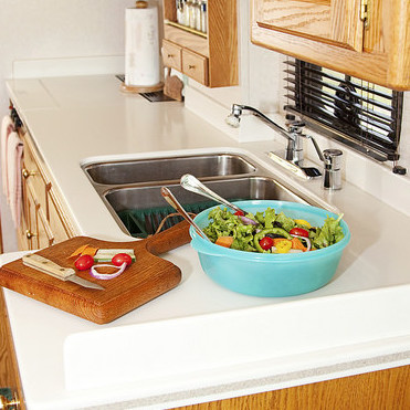 A photo of an RV kitchen with a salad and cutting board in the countertop. 