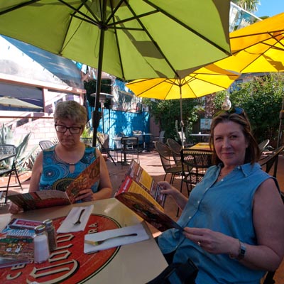 Two women sitting at patio table, holding and reading magazines. 
