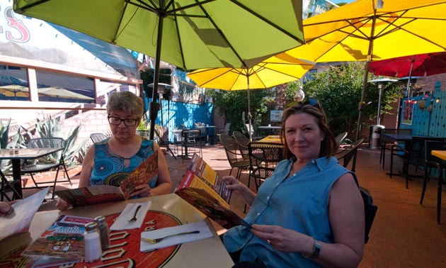 Two women sitting at patio table, holding and reading magazines. 