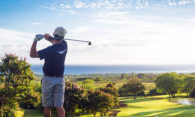 Man golfing with ocean vista in background. 