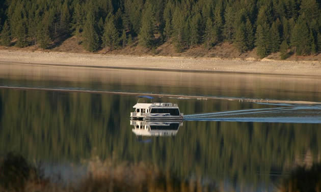 Houseboat on calm water that mirrors the shore and trees