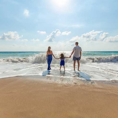 Family enjoying day at beach, wading into incoming tide. 