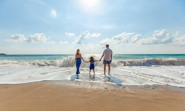 Family enjoying day at beach, wading into incoming tide. 