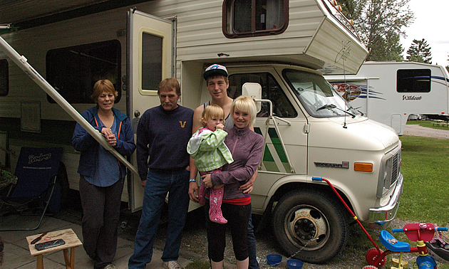 Grandparents, young couple and toddler stand beside their RV.