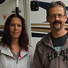 Couple stands with their German shepherd beside their motorhome.