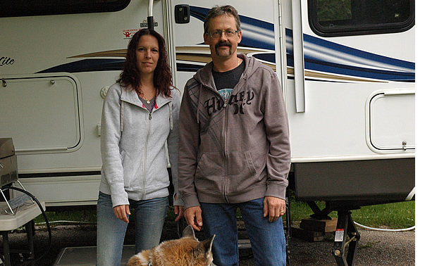 Couple stands with their German shepherd beside their motorhome.