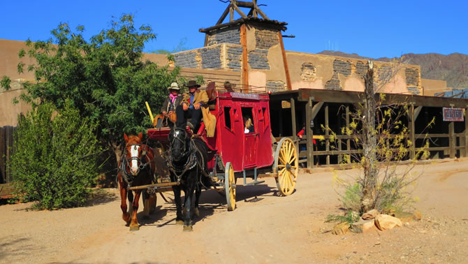 A stagecoach led by horses is rolling down the street of an Old Western town.