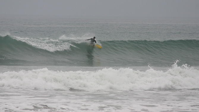 Picture of a surfer in the ocean, riding a wave on a grey, overcast day. 
