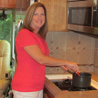 Sylvia stands in her RV kitchen smiling at the camera while cooking in a saucepan.