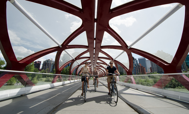 Three bikers smile as they pedal beneath the futuristic red 