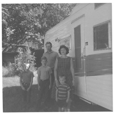 B&W picture of family (mom, dad, 3 boys) standing in front of Tee Pee trailer. 