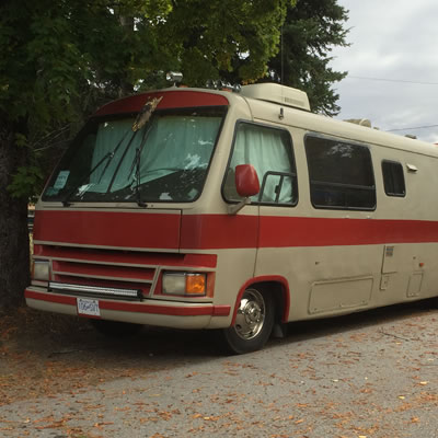 A large tan and brown motorhome parked on a leafy street, 