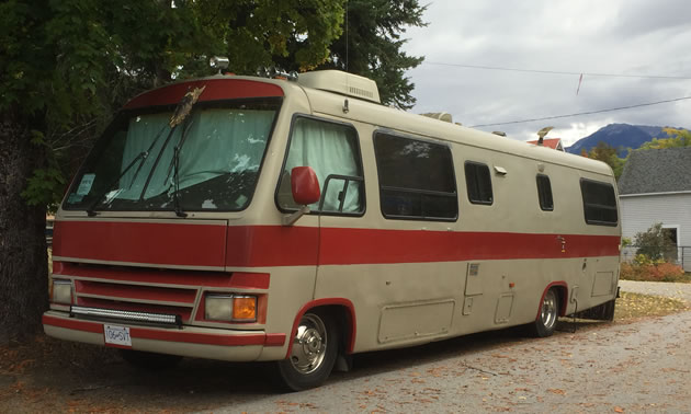 A large tan and brown motorhome parked on a leafy street, 