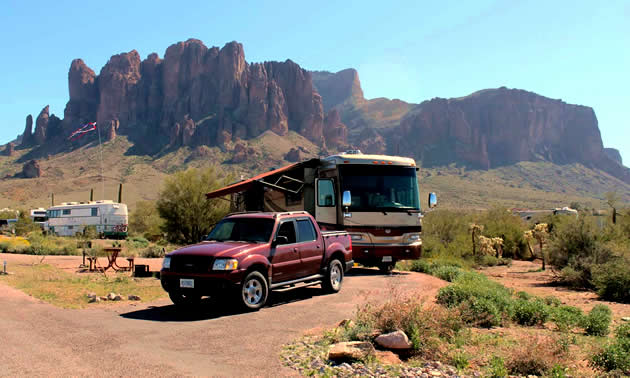 A red truck and brown RV are parked in front of Arizona's Superstition Mountains