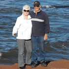A man and woman wearing blue and white sweaters stand in front of the ocean.